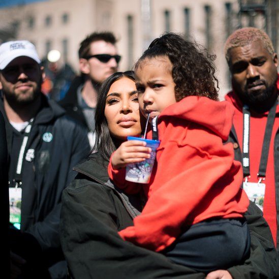 Kardashian, Holding North, with Kanye in background at event