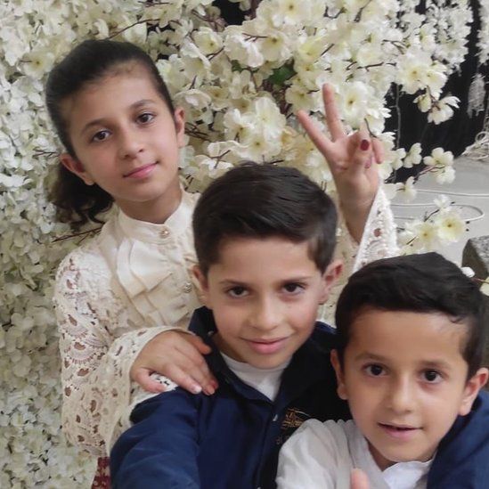 Three children pose in front of cherry blossom