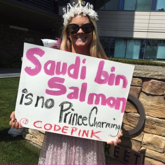A protesters sign says the guest is "no prince charming"