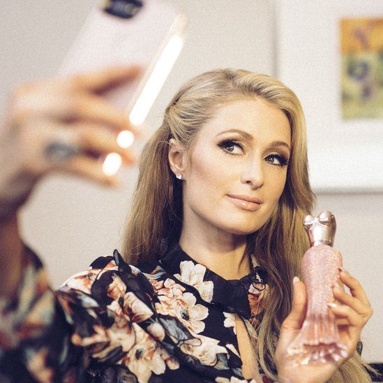 Photograph shows Paris Hilton taking a photograph with her fragrance bottle