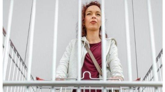 Woman looks through bars of empty shopping trolley