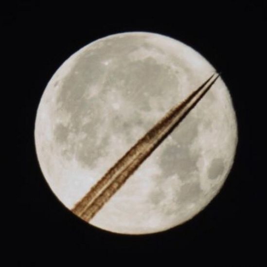 The supermoon appears with trails from an aircraft juxtaposed against it