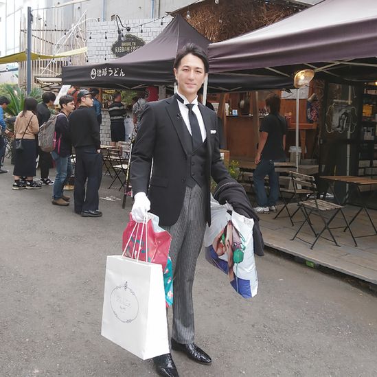 Yuichi Ishii vestido elegantemente de fraque e luvas brancas, carregando sacolas de compras