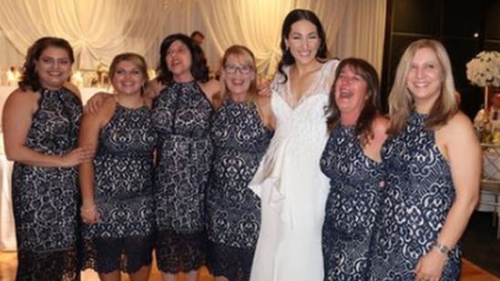 Six wedding guests in identical dresses pose for a photograph with the bride