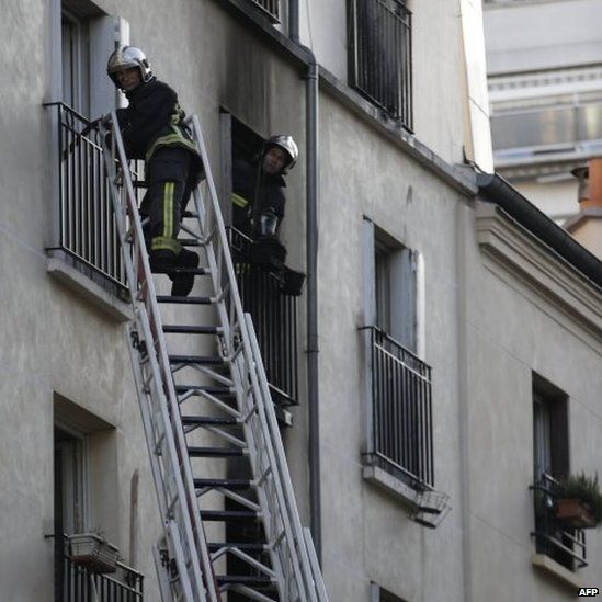 Firefighters use ladders to check the burnt apartment