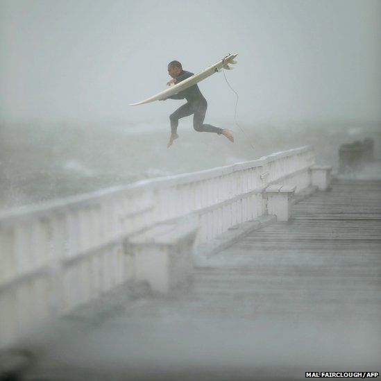 A surfer jumps off the pier into Port Phillip Bay