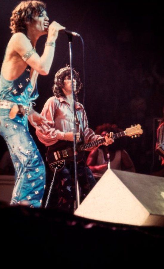 Mick Jagger and Keith Richards performing onstage in a blue jumpsuit with stars and silver shirt