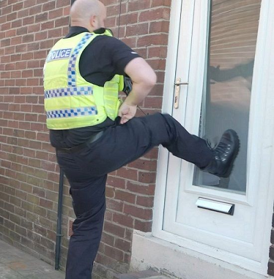 Northumbria Police officer kicking in a white UPVC door with a clear central panel