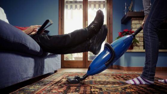 Un hombre sentado en un sof&aacute; mientras otra persona limpia.