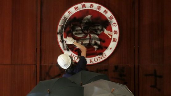 The emblem of Hong Kong in the legislative chamber is spray-painted black by one protester, buoyed by three people holding umbrellas behind him.