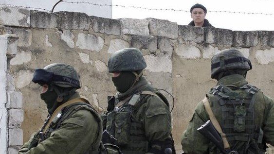 A Ukrainian serviceman (rear) looks at uniformed men, believed to be Russian servicemen, standing guard at a Ukrainian military base in a village outside Simferopol, Crimea, 6 March 2014