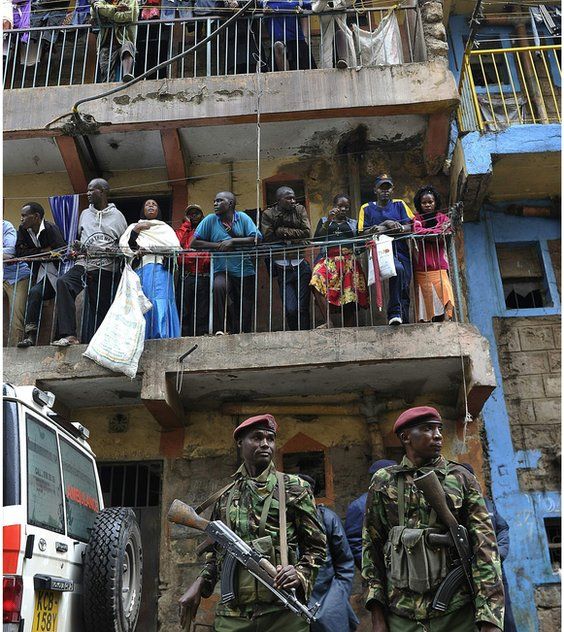 People crowd on balconies watching two armed soldiers in the street