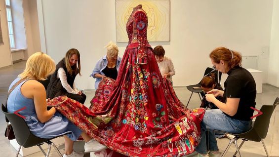 A group of women are embroidering a long red dress 