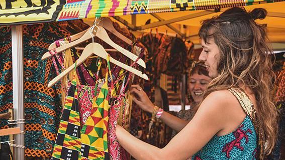 Ruby Maya looking through bright clothing on hangers at her festival stall 