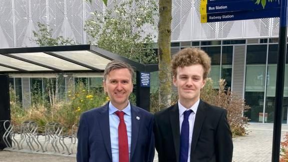 Andrew Pakes and Sam Carling standing under sign saying "bus station", "railway station"