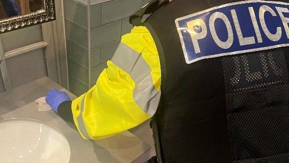 A police officer carrying out a drug wipe around a washroom basin