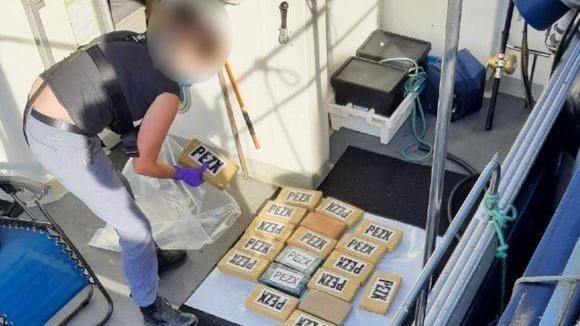 An investigator on board a boat deck, looking at about 20 brown packages measuring about 10in by 5in by 2in each