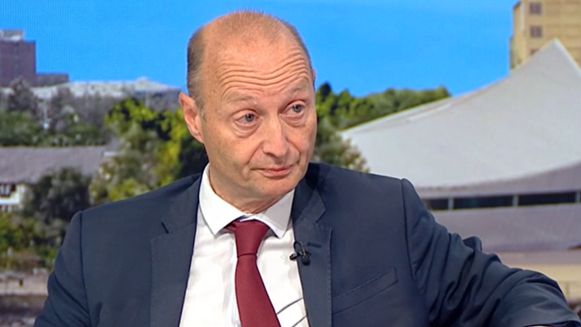 Paul Waugh, wearing a claret tie and navy blue suit sits in the BBC Breakfast studio