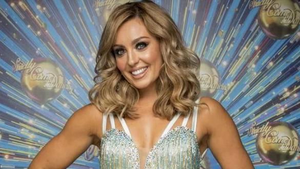 Amy Dowden looking at the camera in a silver sparkly dress with Strictly Come Dancing logo behind her