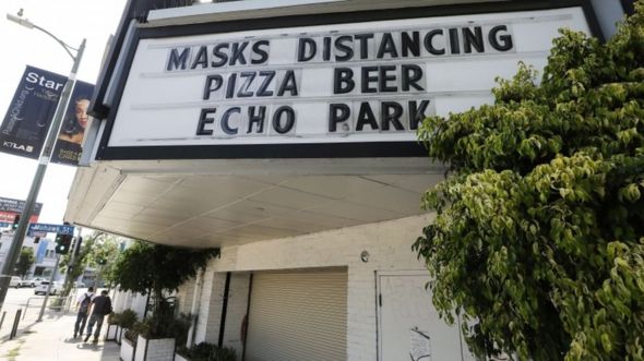 A sign reading "Masks Distancing Pizza Beer" is displayed above a restaurant and bar on Sunset Boulevard amid the COVID-19 pandemic on June 29, 2020 in Los Angeles