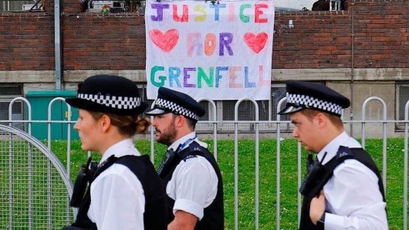 Police officers walk past a poster hanging outside a building calling for 'Justice for Grenfell'