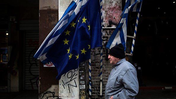 Man walking past Greek and EU flags