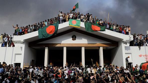 Anti-government protestors display Bangladesh's national flag as they storm Prime Minister Sheikh Hasina's palace in Dhaka on August 5, 2024. Bangladesh army chief Waker-Uz-Zaman spent nearly four decades rising to the top of the military and said on August 5, he was "taking full responsibility" after Prime Minister Sheikh Hasina was ousted and fled