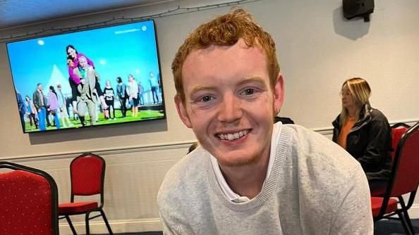 Laim Carr sitting in a pub and smiling at the camera. He is wearing a grey jumper