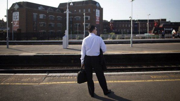 A man stands on a train platform with his back to the camera