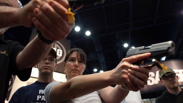 Attendees hold handguns in the Sig Sauer booth during the 2013 NRA Annual Meeting and Exhibits at the George R Brown Convention Center 4 May 2014