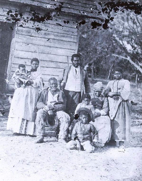 Fotografia de família de escravos nos Estados Unidos - mulher com criança no colo, senhor sentado, homem adulto em pé, duas mulheres e duas crianças