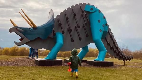 A child approaches a steel dinosaur