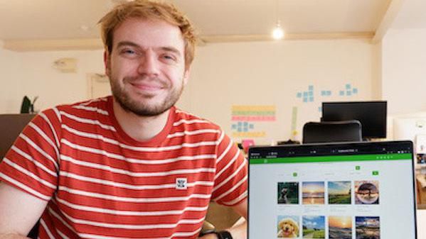 Dylan McKee smiling in a red and white striped t-shirt beside a laptop with pictures of sunsets and dogs and landscapes