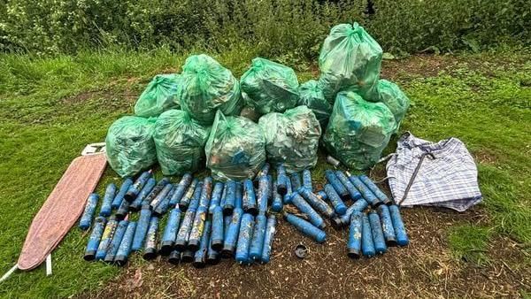 Blue canisters laid down on the grass next to green bin bags 