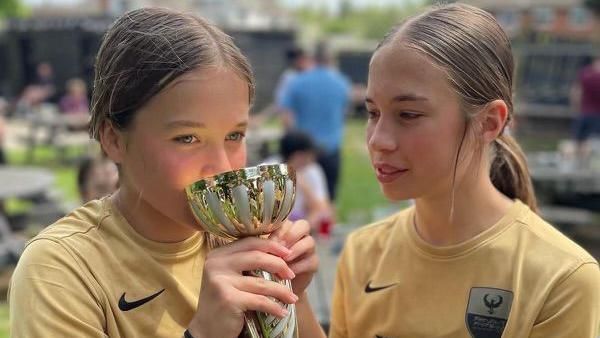 Two girls kissing a youth football cup