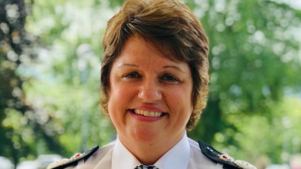 A woman with short brown hair, Pam Kelly, smiling at the camera. She is in a police uniform