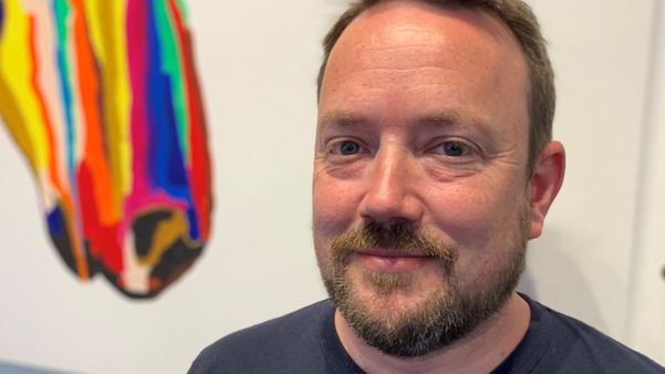 A man with short hair and a neat beard looks at the camera