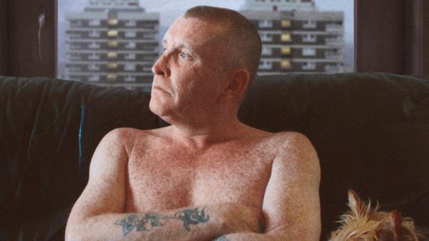  Joe McNally in The Flats pictured topless on sofa with dog and New Lodge flats visible through window behind him
