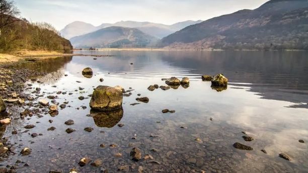 Ennerdale Water with boulders in the foreground and with the sun reflecting on the water 