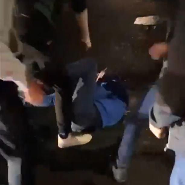Still from the social media video showing a man in a blue jumper lying on the ground being kicked by a group 