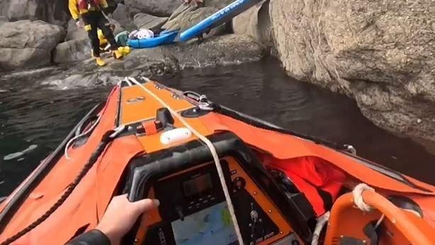 A view from the rescue lifeboat showing crew members assisting Mr Bascombe on rocks