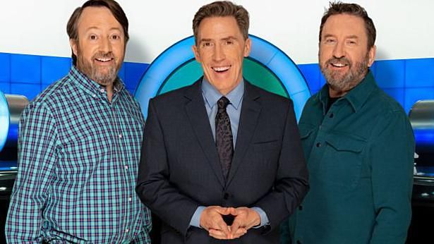 Comedian David Mitchell dressed in a shirt, show host Rob Brydon smiling and dressed in a suit and another comedian Lee Mack dressed in a shirt for a promo shot for BBC hit TV show Would I Lie To You