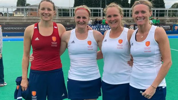 Lucy Field and three teammates standing on a hockey pitch after a game. They have their arms around each other and are all wearing vest tops with "England Hockey" emblem on them. 