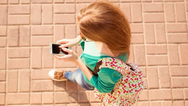 Mujer joven andando por la calle con el celular.