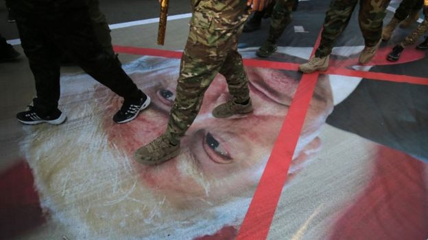 Integrantes de milícia iraquiana caminham sobre foto de Trump em Bagdá nesta segunda-feira