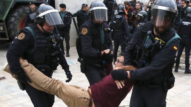 three Guardia Civil in riot gear carrying a man in civilian clothes