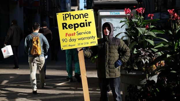 Un hombre sostiene un aviso de reparación de iPhones
