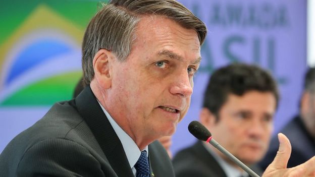 Bolsonaro fala no microfone em reunião, com Moro no plano de fundo