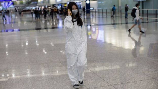 A traveller wearing a full protective gown walks into the arrival hall at Hong Kong International Airport