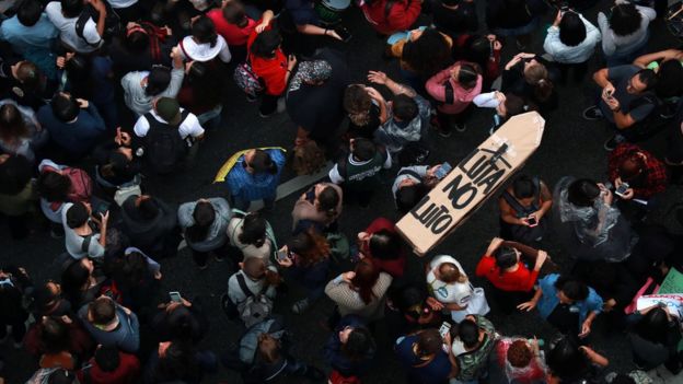 Foto aérea mostra dezenas de manifestantes em avenida de São Paulo, com caixa de papelão em formato de caixão dizendo: "Luta no luto"